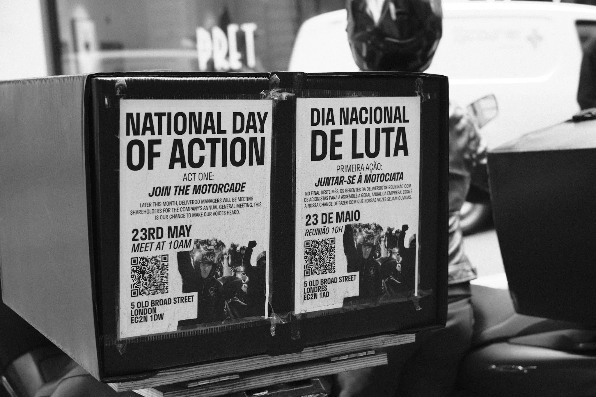 Two posters taped to the side of a courier's delivery box, one in English and one in Portuguese, headed National Day of Action and Dia Nacional de Luta, calling a motorcade to 5 Old Broad Street on 23rd May.