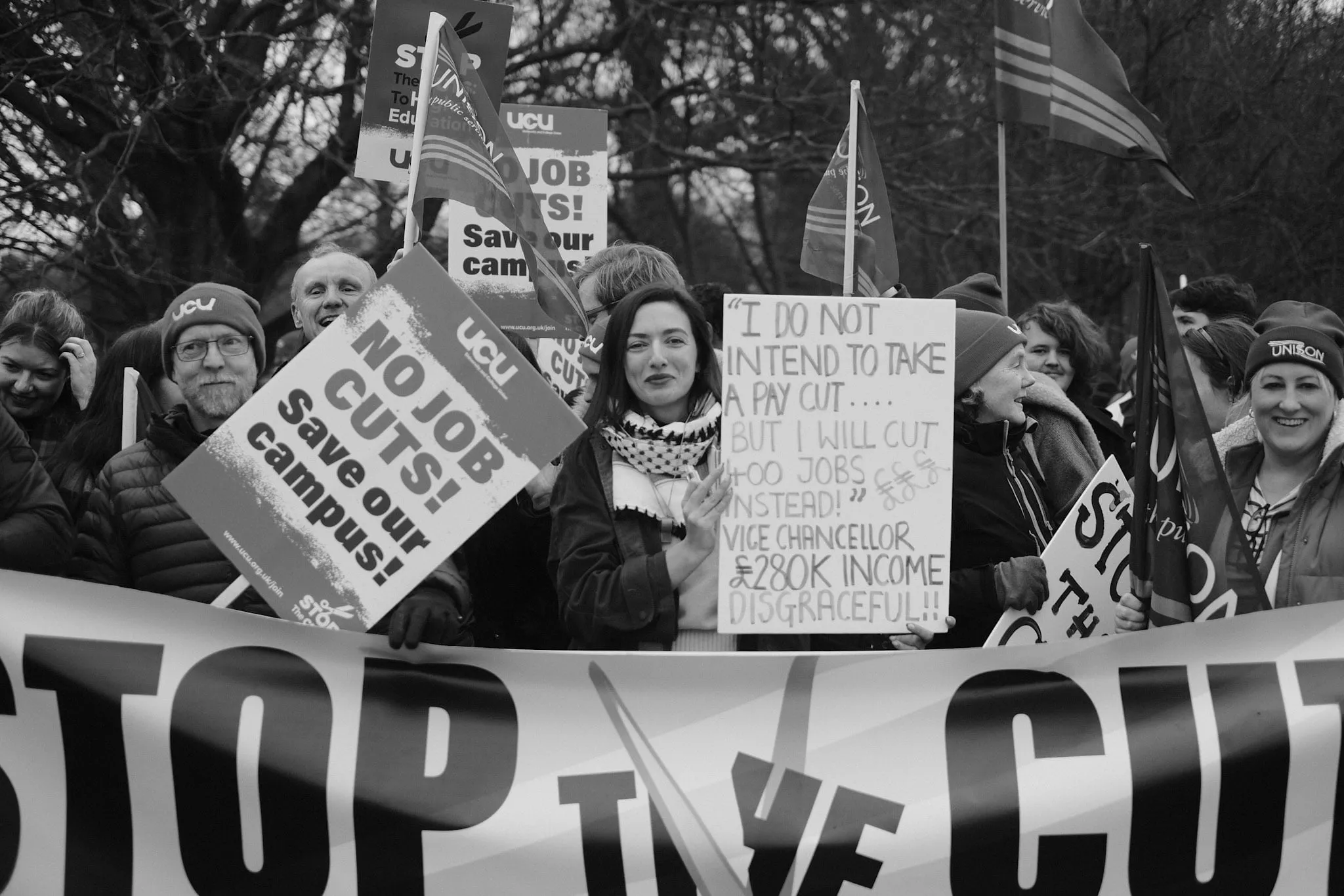 A crowd stands behind a STOP THE CUTS banner, one handwritten placard quoting the Vice-Chancellor — I do not intend to take a pay cut, but I will cut 400 jobs instead — beside union flags.