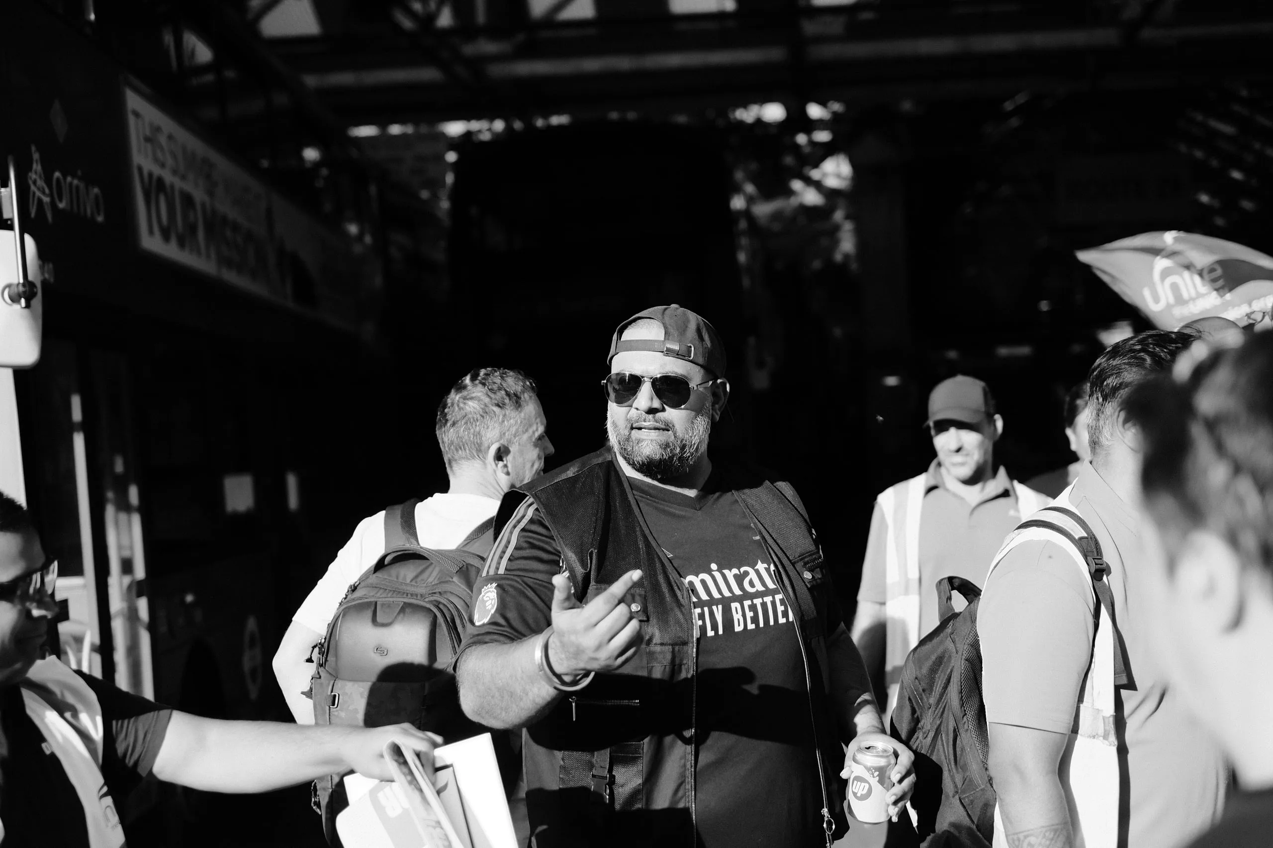 A striker in sunglasses and a backwards cap talking and gesturing to others in the crowd at the garage entrance.