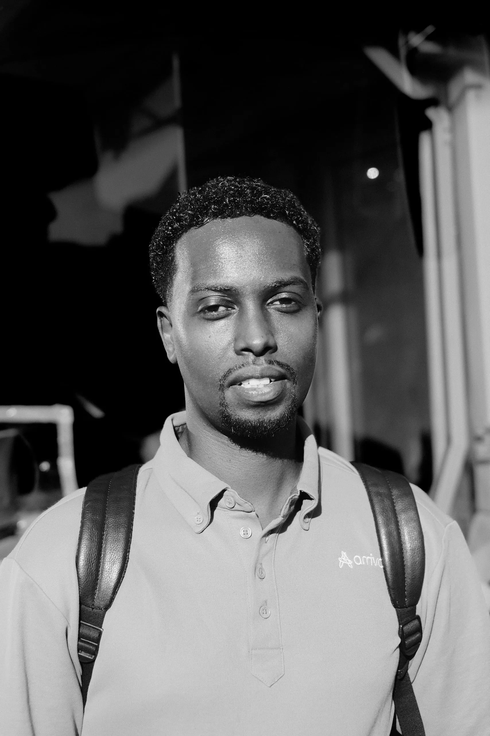 A driver in an Arriva polo shirt with a backpack, looking into the camera.